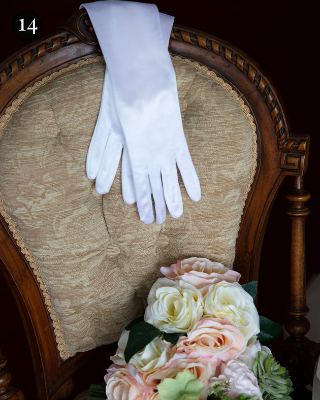 Women's long opera satin gloves in white laid out on a chair with a bouquet of flowers