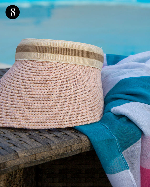 Women's straw sun visor with ribbon band in pink next to a pool