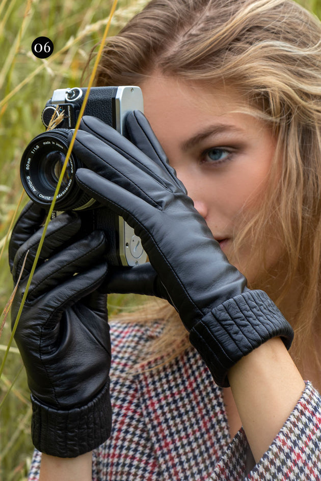 close up image of a woman wearing black leather gloves with ribbed cuffs holding a film camera