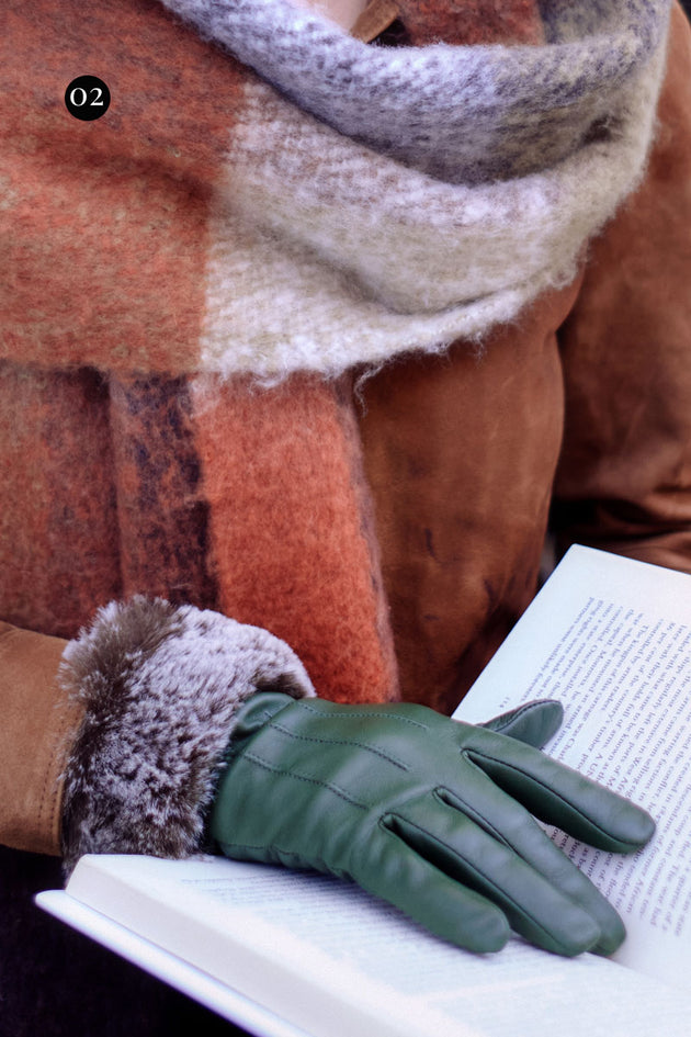 Close up shot of a woman wearing green faux fur cuff leather gloves whilst reading a book