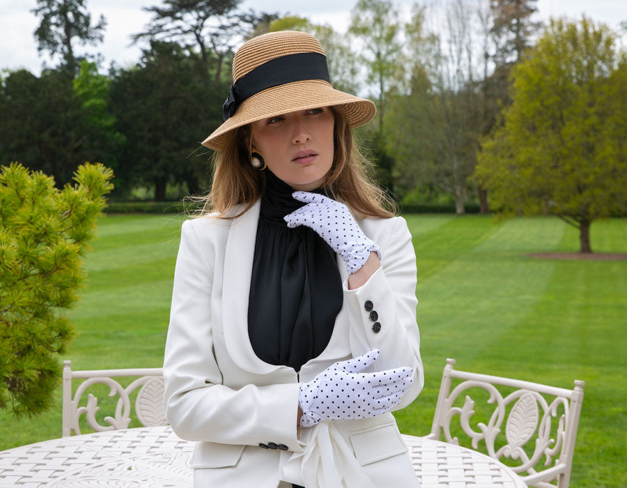 Woman wearing a straw sun hat and spotty cotton gloves with a white suit and black blouse at a country park