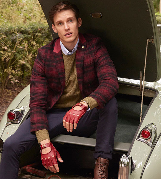 Man wearing red fingerless leather driving gloves sat in the boot of a classic car