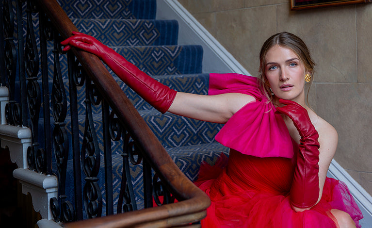 Woman wearing long red leather gloves and red and pink ballgown sat on blue steps