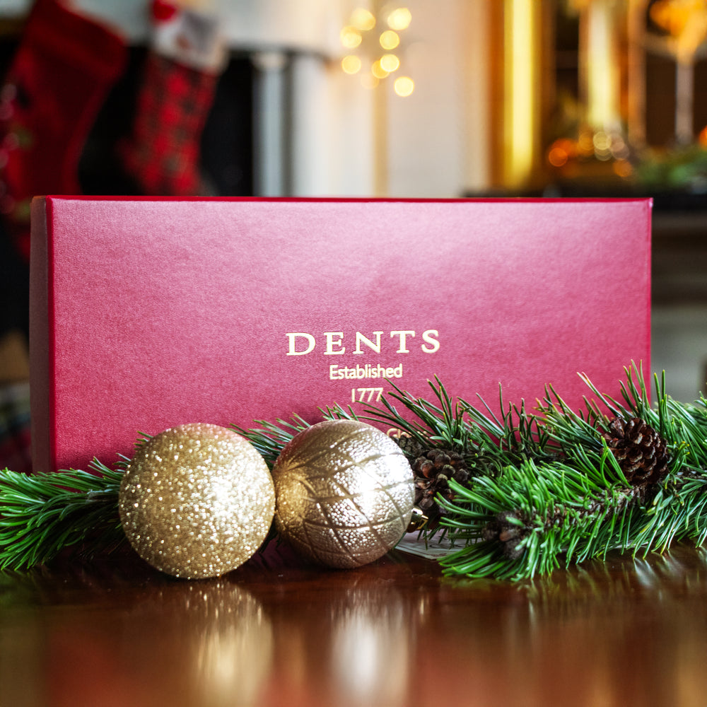 Dents gift box with gold Christmas baubles and green foliage with festive background