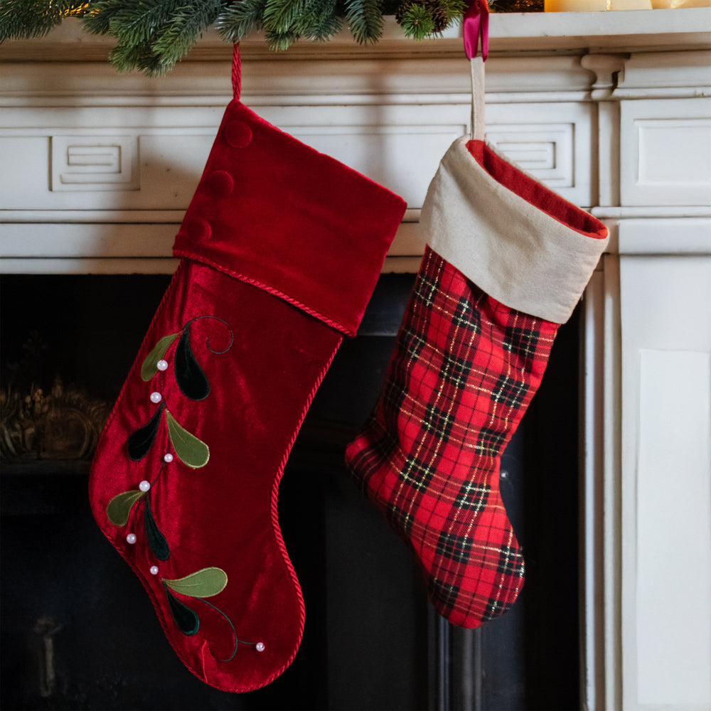 Two red Christmas stockings hanging from a festive fireplace