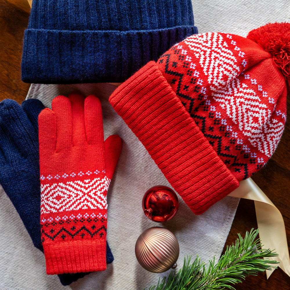 Men's navy knitted gloves and matching beanie hat with women's patterned red knitted gloves and matching bobble hat with festive background