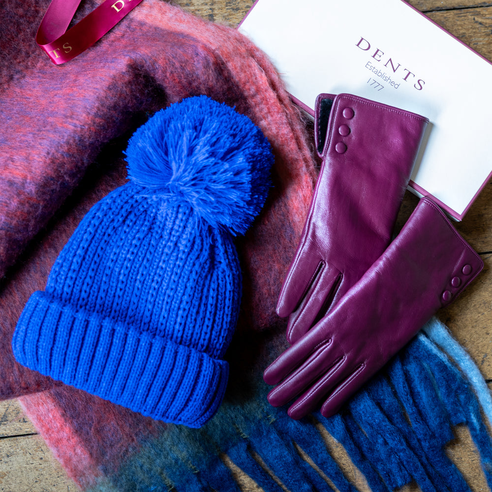 Women's Christmas gifts, including purple leather gloves, blue knitted bobble hat and a blanket scarf with a Dents gift box