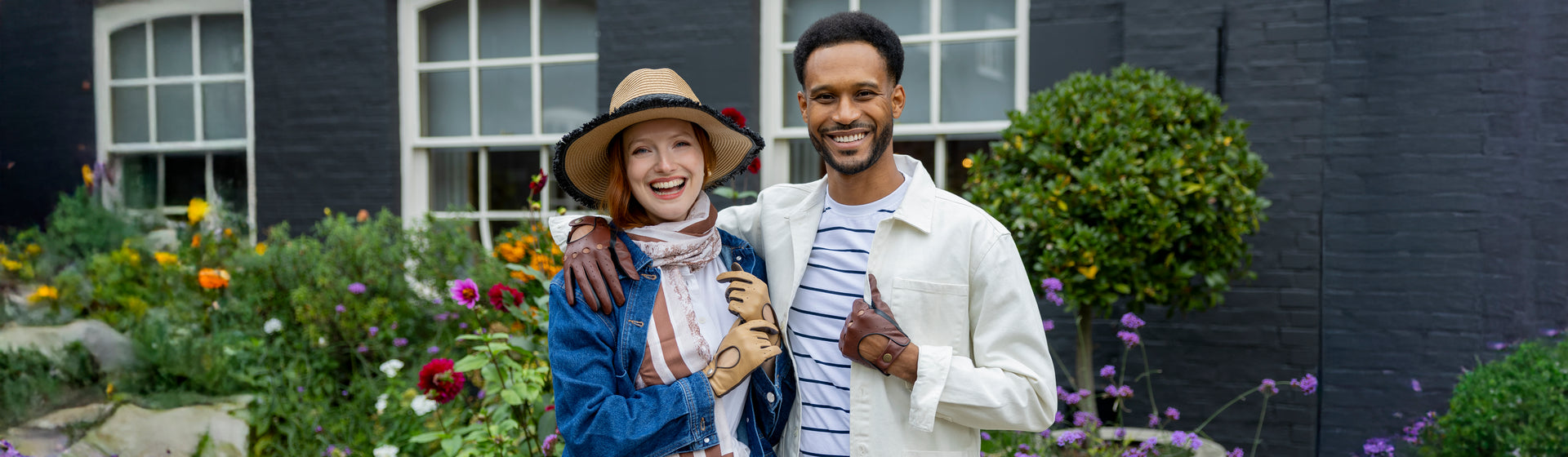 Two people standing together in a garden wearing summer hat, scarves and gloves