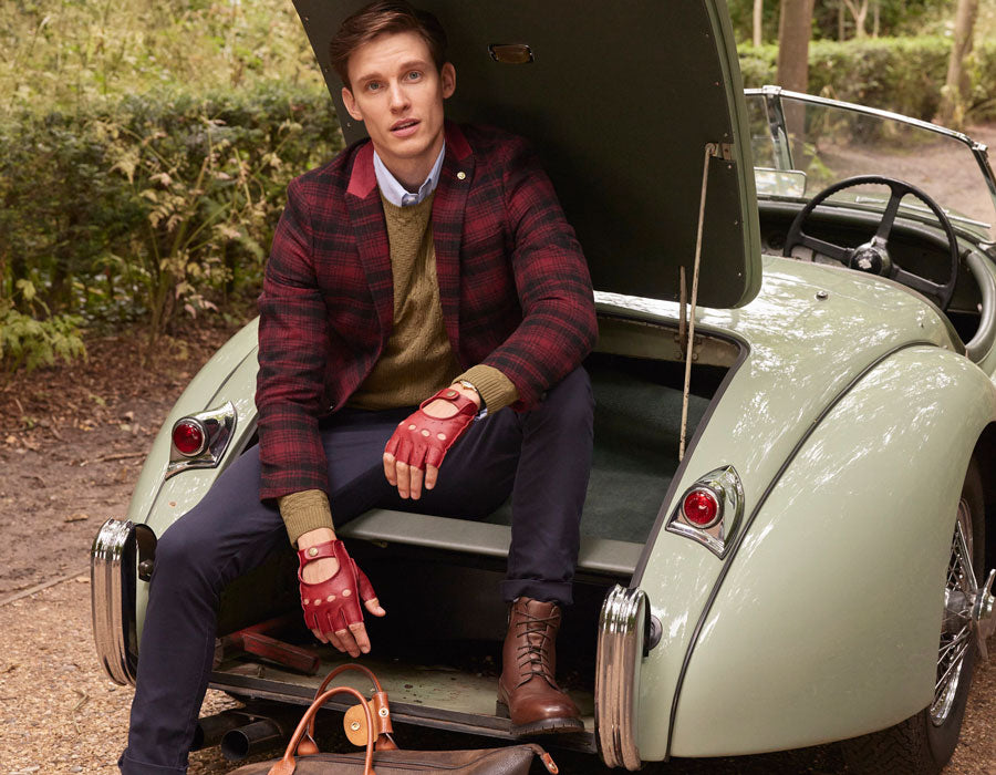 Man sitting in the open door of a vintage car wearing red leather fingerless driving gloves