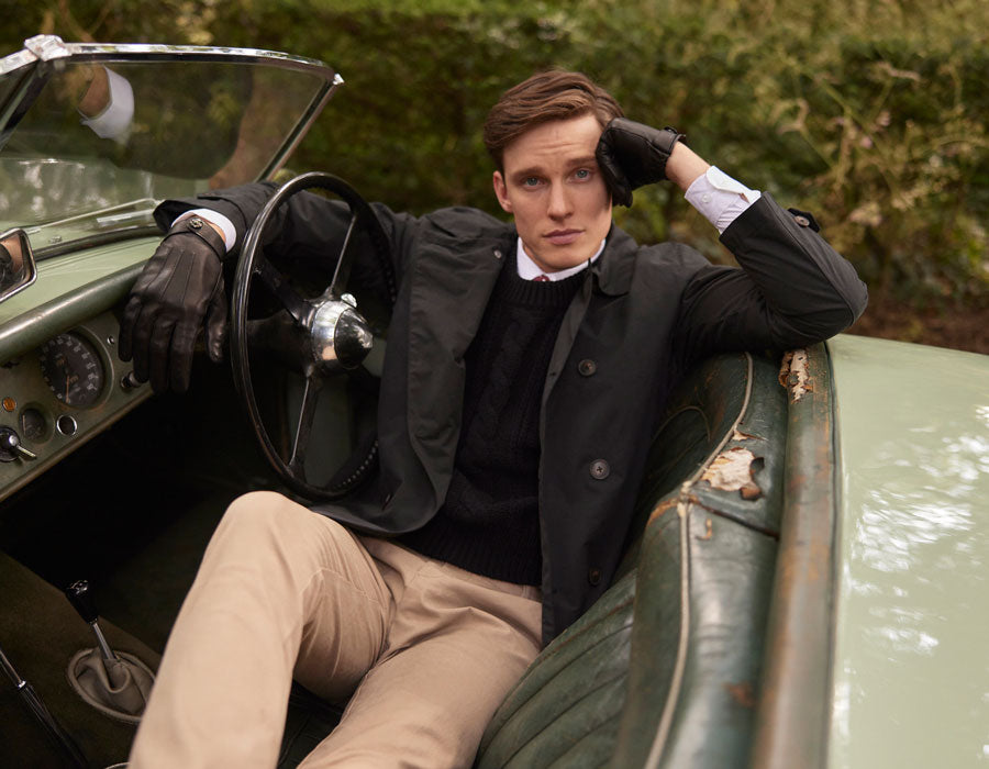 Man wearing heritage leather driving gloves in black sitting behind a wheel of a classic car