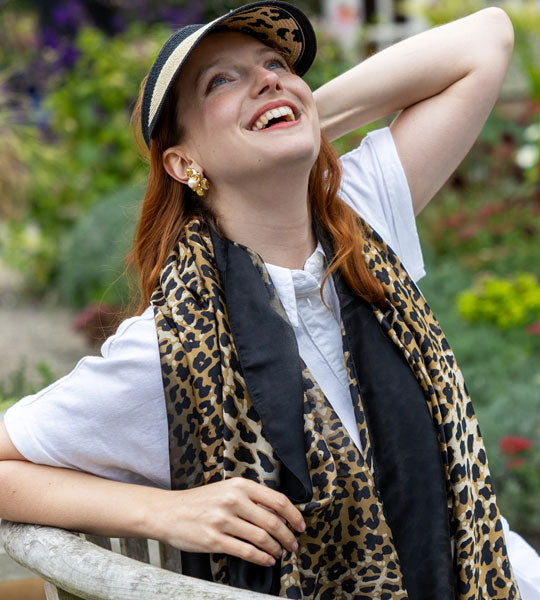 Woman wearing a leopard print scarf and hat in a garden