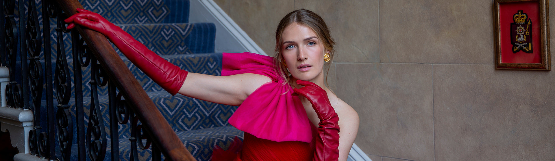 Woman wearing long red leather gloves and a pink and red ballgown sat on blue steps
