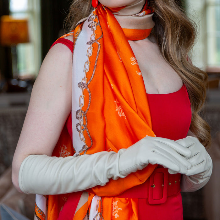 Woman wearing nautical print silk-like lightweight scarf in orange with long leather ivory gloves